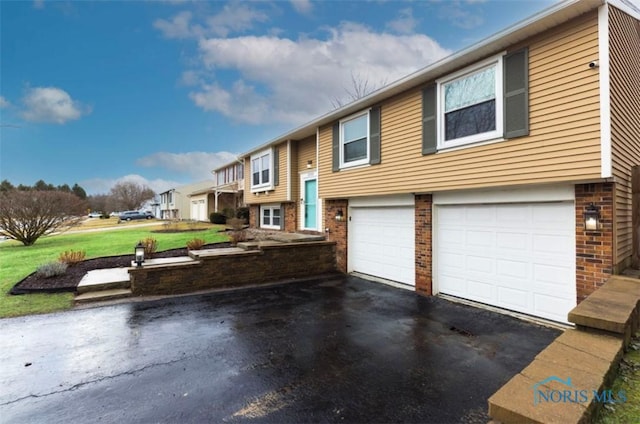 split foyer home with a garage, a front lawn, aphalt driveway, and brick siding