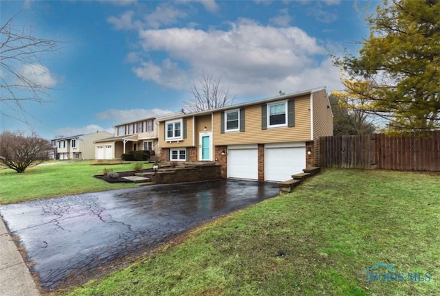 split foyer home with aphalt driveway, an attached garage, brick siding, fence, and a front lawn