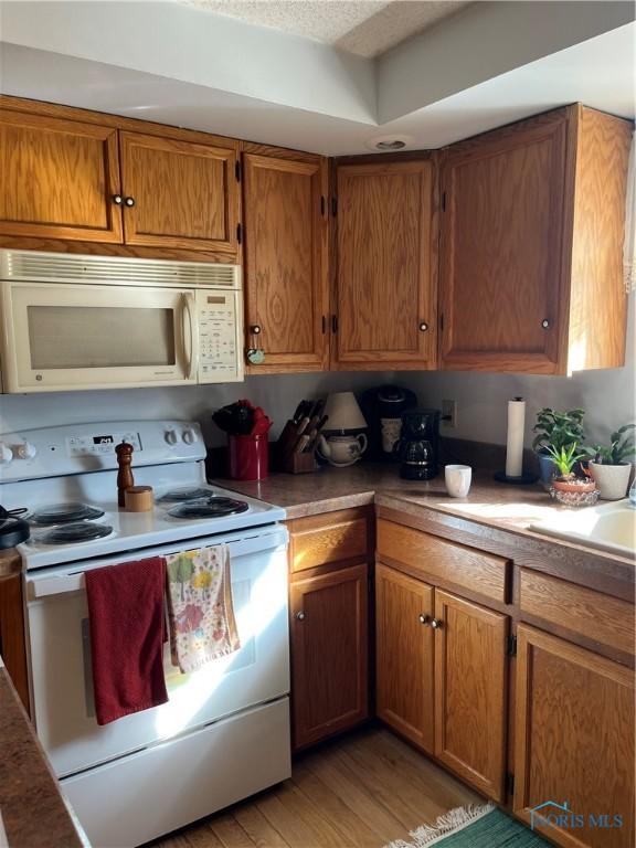 kitchen featuring white appliances, light wood finished floors, a sink, and brown cabinetry