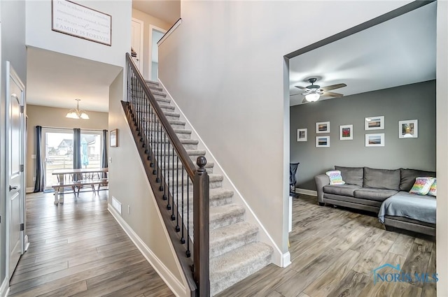 stairs featuring ceiling fan with notable chandelier, baseboards, and wood finished floors