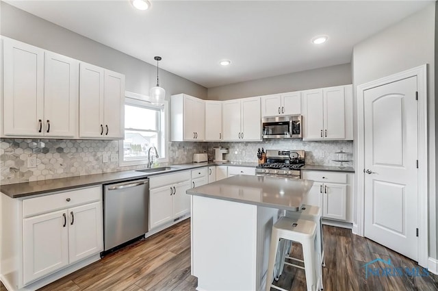 kitchen featuring appliances with stainless steel finishes, dark wood-style flooring, a center island, white cabinetry, and a sink