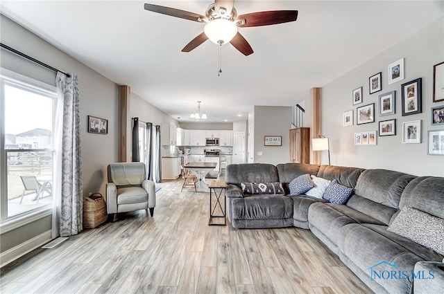 living room featuring a healthy amount of sunlight, light wood finished floors, baseboards, and ceiling fan with notable chandelier