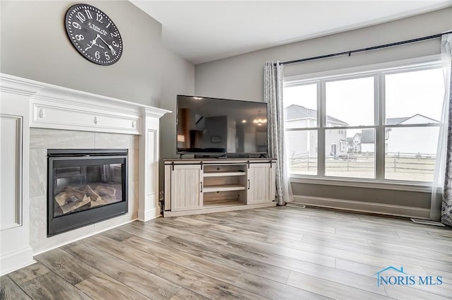 unfurnished living room with a tile fireplace, baseboards, and light wood finished floors