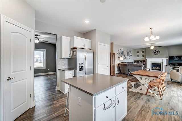 kitchen with white cabinets, stainless steel fridge with ice dispenser, dark wood-type flooring, a fireplace, and ceiling fan with notable chandelier