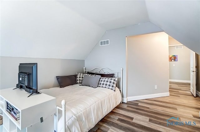 bedroom with vaulted ceiling, wood finished floors, visible vents, and baseboards