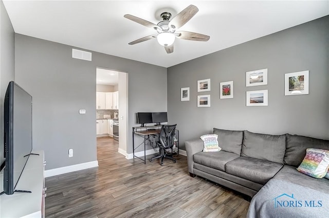 living room with a ceiling fan, visible vents, baseboards, and wood finished floors