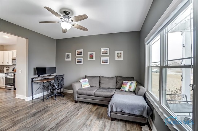 living room featuring a healthy amount of sunlight, a ceiling fan, baseboards, and wood finished floors