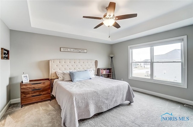 bedroom with a tray ceiling, carpet flooring, visible vents, and baseboards