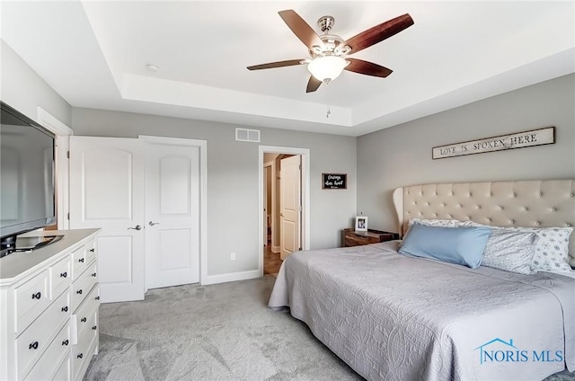 bedroom featuring baseboards, visible vents, light colored carpet, ceiling fan, and a tray ceiling