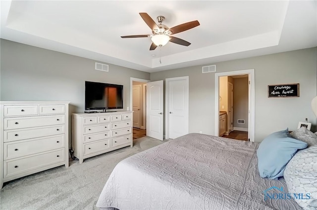 bedroom featuring connected bathroom, a raised ceiling, visible vents, and light colored carpet