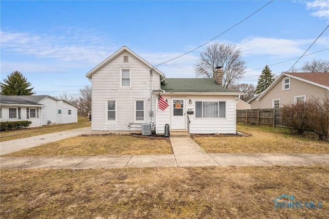 traditional-style home with central air condition unit, a chimney, fence, and a front yard