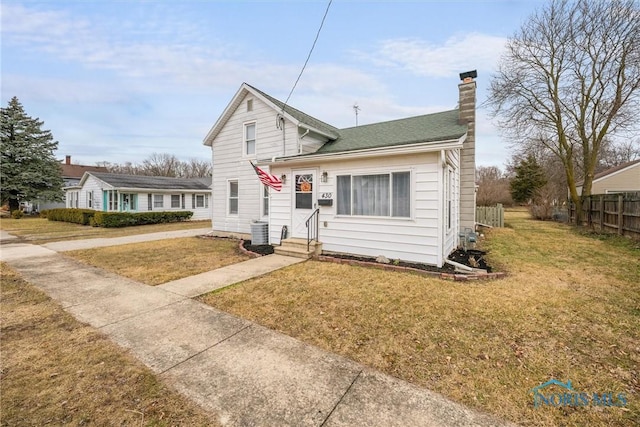 view of front of home with entry steps, central AC unit, fence, a front lawn, and a chimney