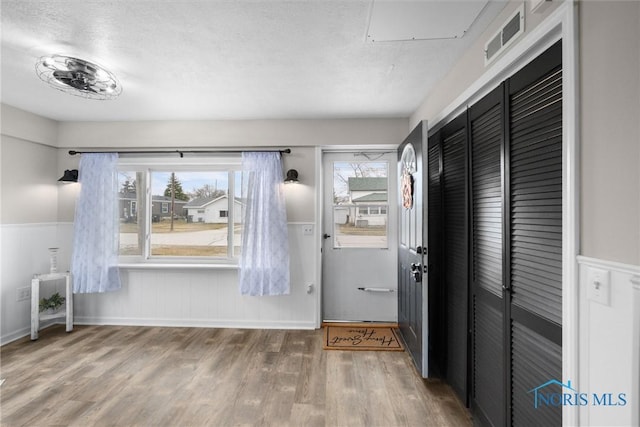 interior space with wainscoting, visible vents, a wealth of natural light, and wood finished floors