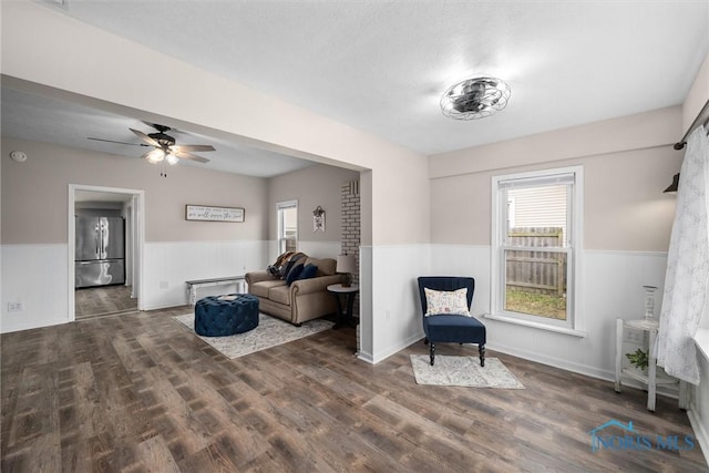 living area featuring ceiling fan, wood finished floors, and wainscoting