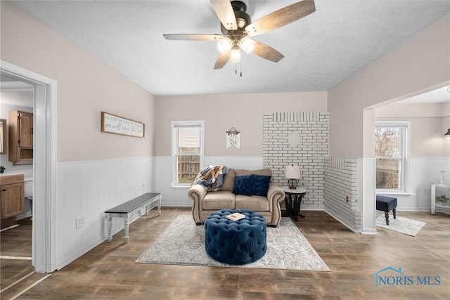 living area with wainscoting, a healthy amount of sunlight, ceiling fan, and wood finished floors