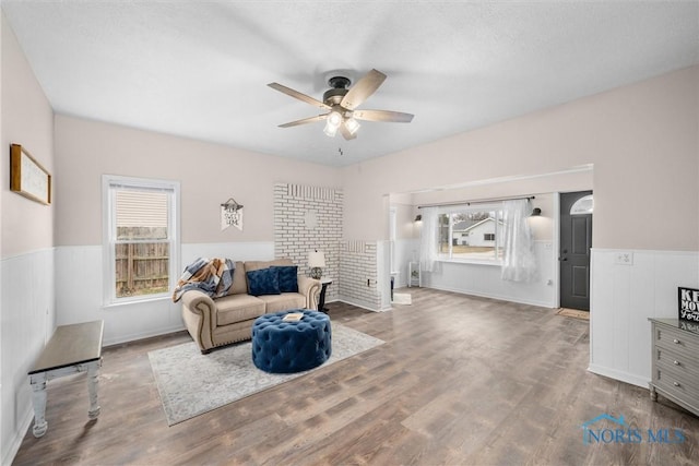 living area with a wainscoted wall, plenty of natural light, and wood finished floors