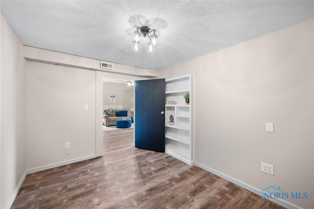 spare room featuring baseboards, a textured ceiling, visible vents, and wood finished floors