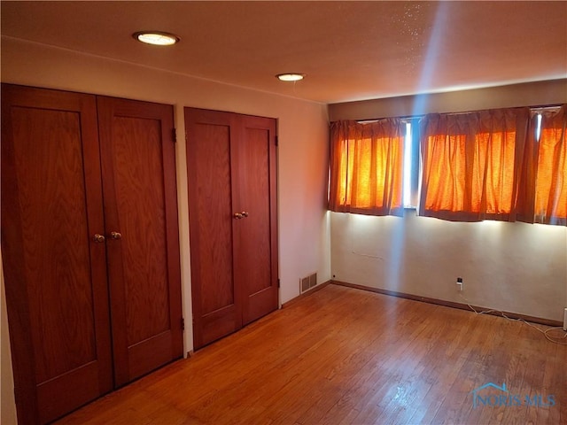 unfurnished bedroom featuring visible vents, baseboards, and wood finished floors