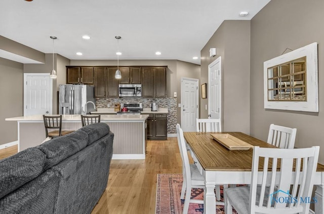 kitchen with stainless steel appliances, light countertops, backsplash, light wood-style floors, and dark brown cabinetry