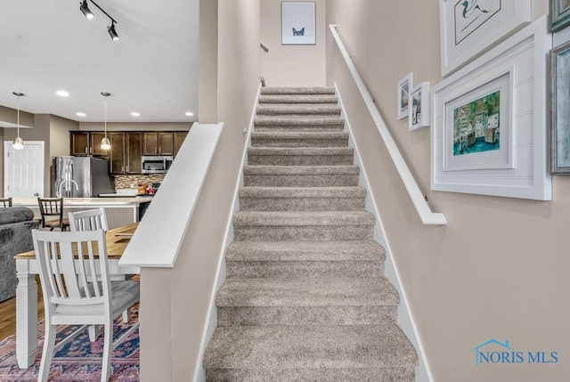 stairway featuring track lighting, recessed lighting, wood finished floors, and baseboards