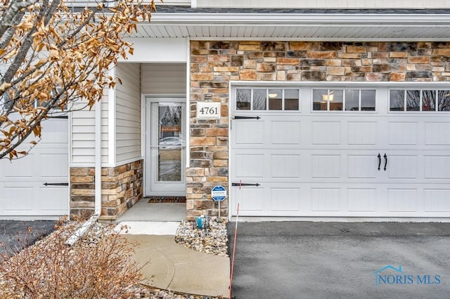 property entrance with driveway, stone siding, and a garage