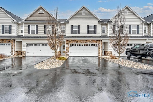 townhome / multi-family property featuring an attached garage, driveway, and stone siding