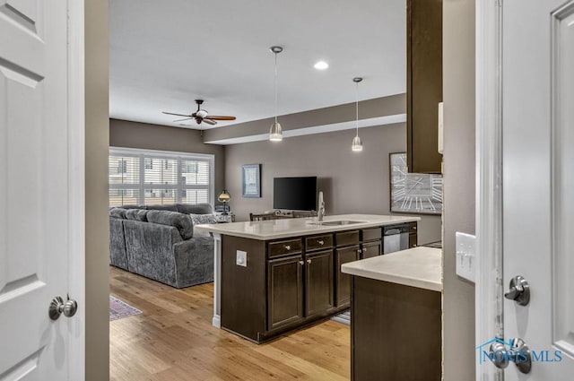 kitchen with light wood finished floors, light countertops, stainless steel dishwasher, a sink, and dark brown cabinets