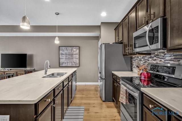 kitchen featuring dark brown cabinetry, tasteful backsplash, a kitchen island with sink, stainless steel appliances, and a sink