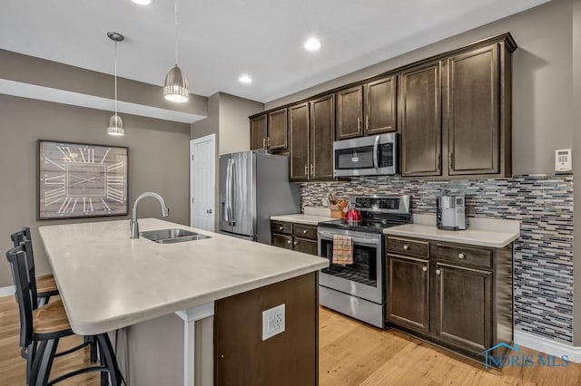 kitchen featuring a center island with sink, appliances with stainless steel finishes, dark brown cabinetry, a sink, and a kitchen breakfast bar