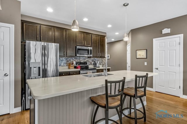 kitchen featuring light wood-style flooring, dark brown cabinetry, a sink, appliances with stainless steel finishes, and decorative backsplash