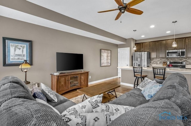 living area with light wood-style floors, baseboards, a ceiling fan, and recessed lighting