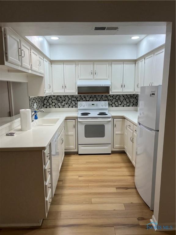 kitchen with light wood-style flooring, under cabinet range hood, white appliances, a sink, and visible vents