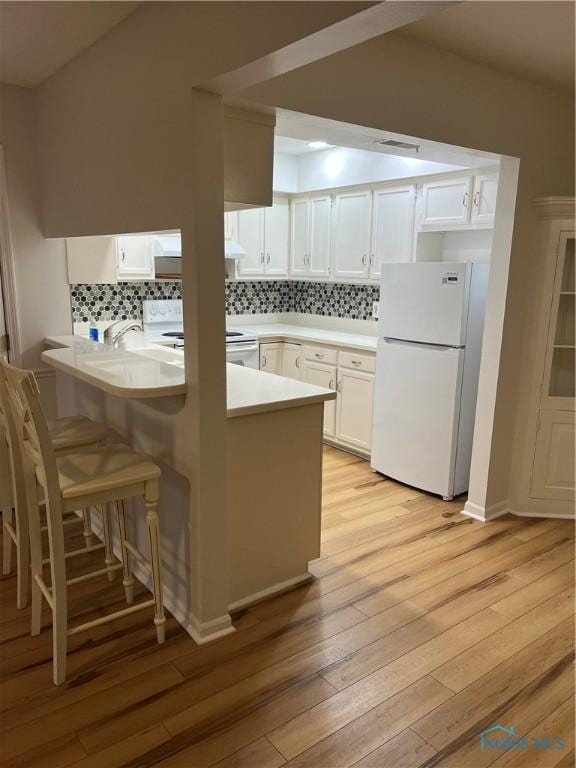 kitchen with light wood-style flooring, decorative backsplash, white cabinetry, white appliances, and a peninsula