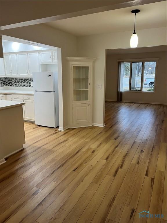 kitchen featuring light wood-type flooring, light countertops, backsplash, and freestanding refrigerator