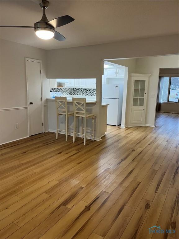 interior space with light wood-style floors, freestanding refrigerator, ceiling fan, and tasteful backsplash