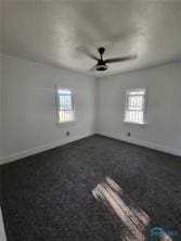 spare room with ceiling fan, baseboards, and dark colored carpet