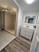 bathroom featuring wood finished floors, tiled shower, and vanity