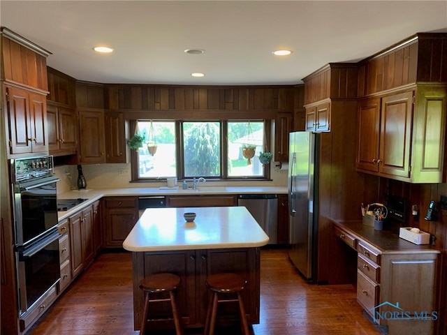 kitchen with a breakfast bar, a sink, a kitchen island, dark wood-style floors, and black appliances