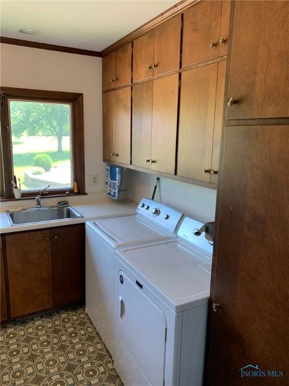 washroom with crown molding, cabinet space, a sink, and washer and clothes dryer