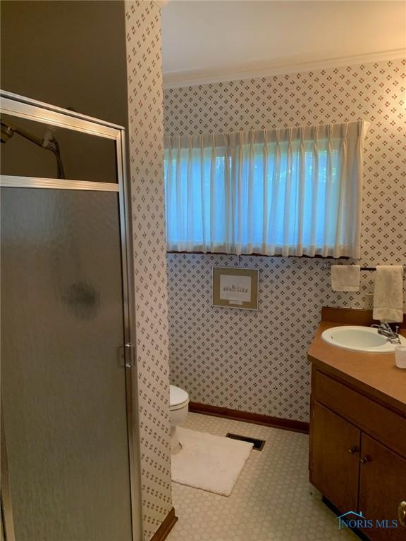 bathroom featuring a stall shower, baseboards, toilet, crown molding, and vanity