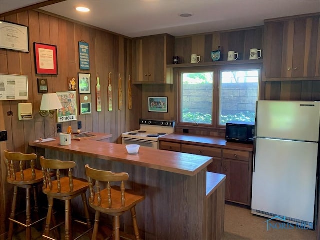 kitchen featuring a breakfast bar area, recessed lighting, a peninsula, white appliances, and wood walls