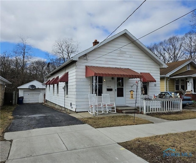 view of front of house featuring a garage, a chimney, aphalt driveway, covered porch, and an outdoor structure