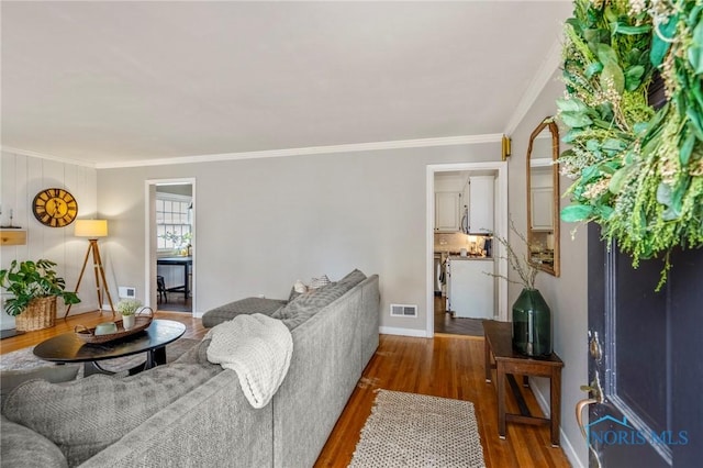 living area with baseboards, crown molding, visible vents, and wood finished floors