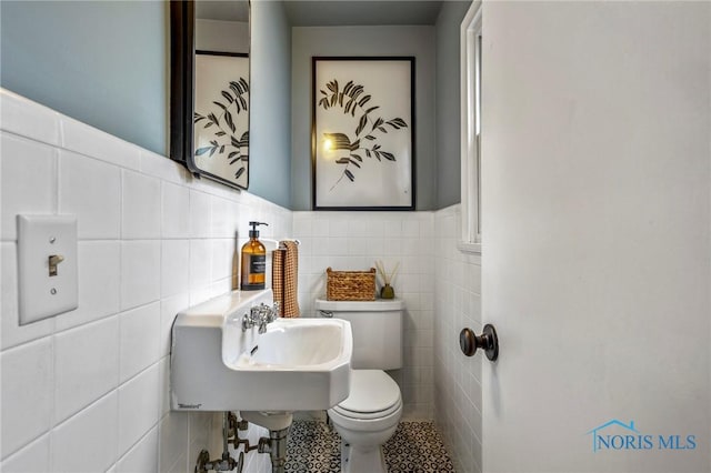 half bathroom with tile walls, toilet, wainscoting, a sink, and tile patterned flooring