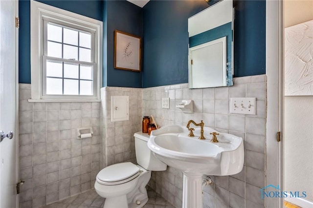 half bathroom featuring wainscoting, tile walls, and toilet