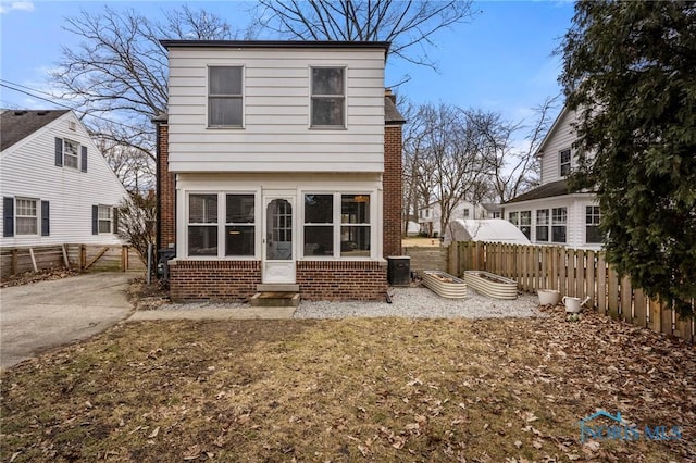 rear view of house with a sunroom, brick siding, and fence