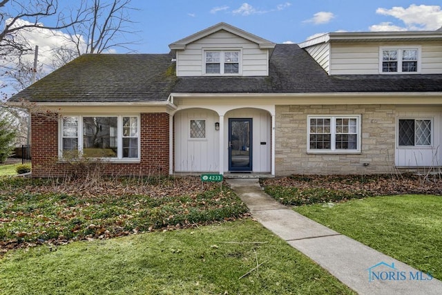 view of front of home with a shingled roof, stone siding, a front lawn, board and batten siding, and brick siding