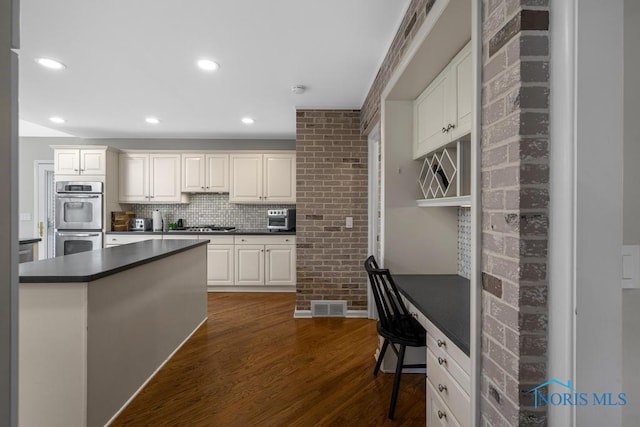 kitchen featuring visible vents, dark countertops, brick wall, dark wood-style flooring, and stainless steel appliances