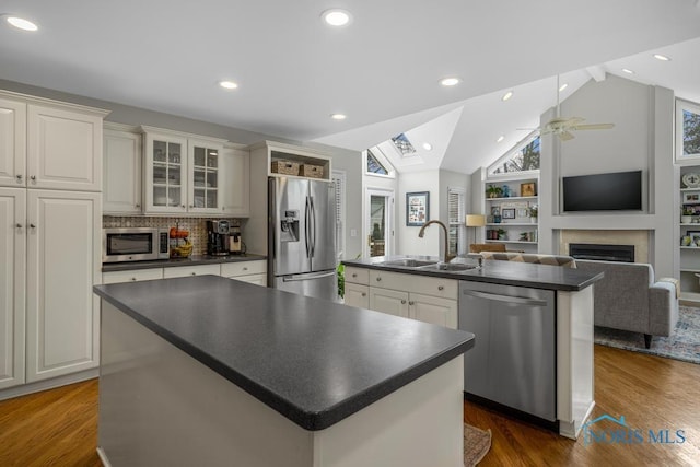 kitchen featuring appliances with stainless steel finishes, dark countertops, a sink, and an island with sink