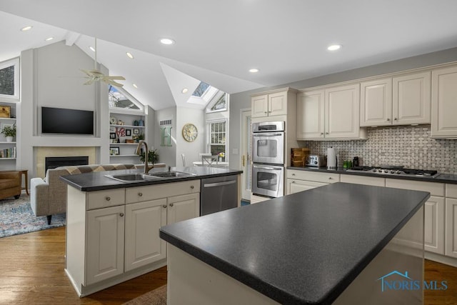 kitchen featuring dark countertops, appliances with stainless steel finishes, a kitchen island with sink, a fireplace, and a sink